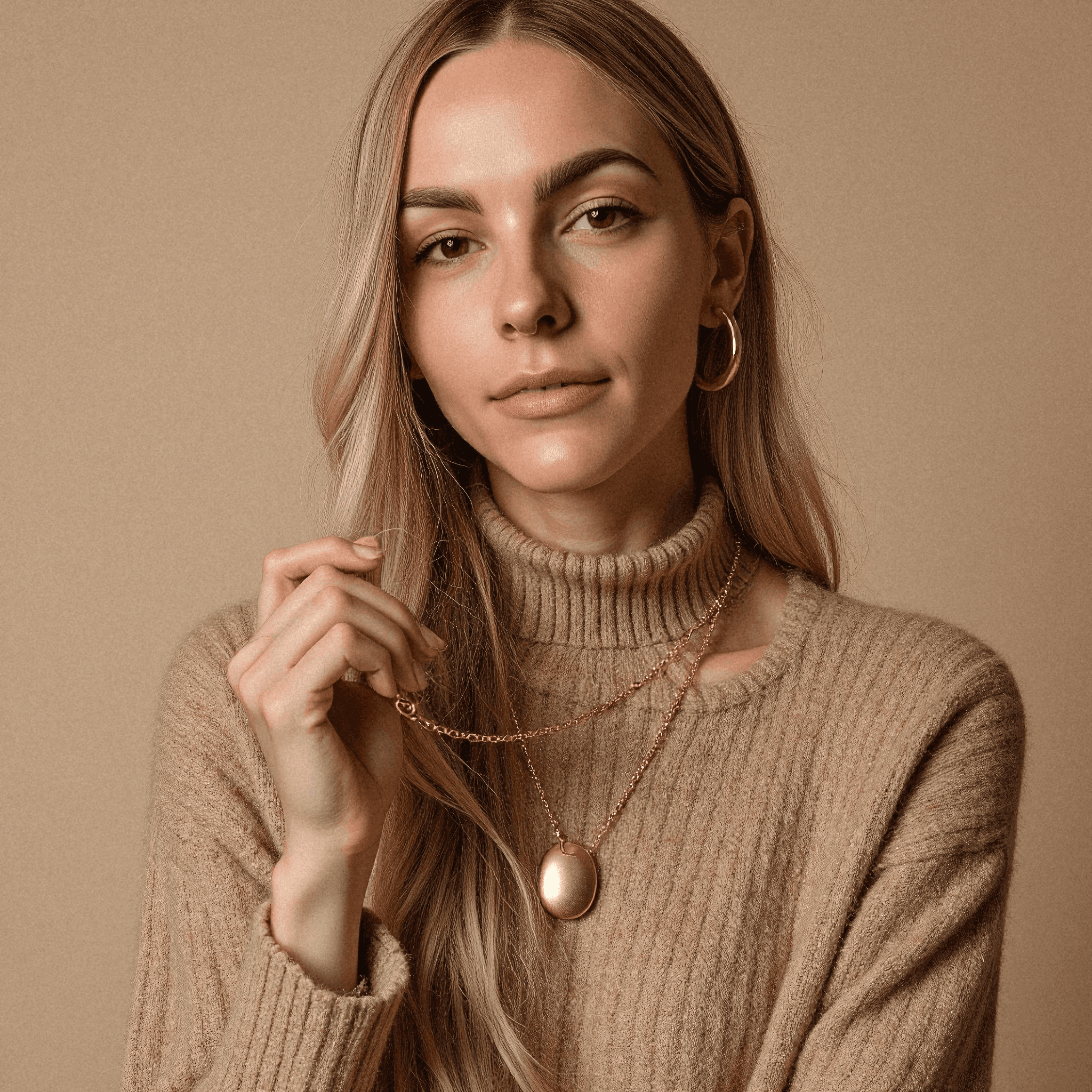 Woman in taupe sweater holding gold pendant